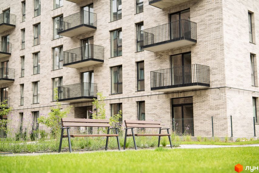 Фасад житлового комплексу WAWEL з балконами та вікнами, зелена прибудинкова територія з лавками.