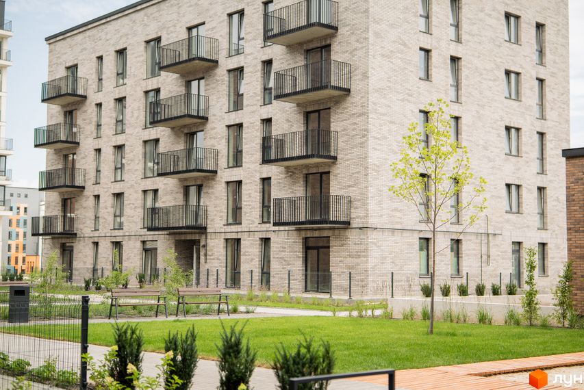 Будинок житлового комплексу WAWEL з цегляним фасадом та балконами. Поруч зелена галявина з лавками та деревами.