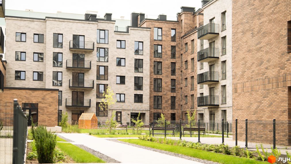 Зовнішній вигляд житлового комплексу WAWEL з цегляними фасадами та балконами. На прибудинковій території розташовані зелені зони та лавки.