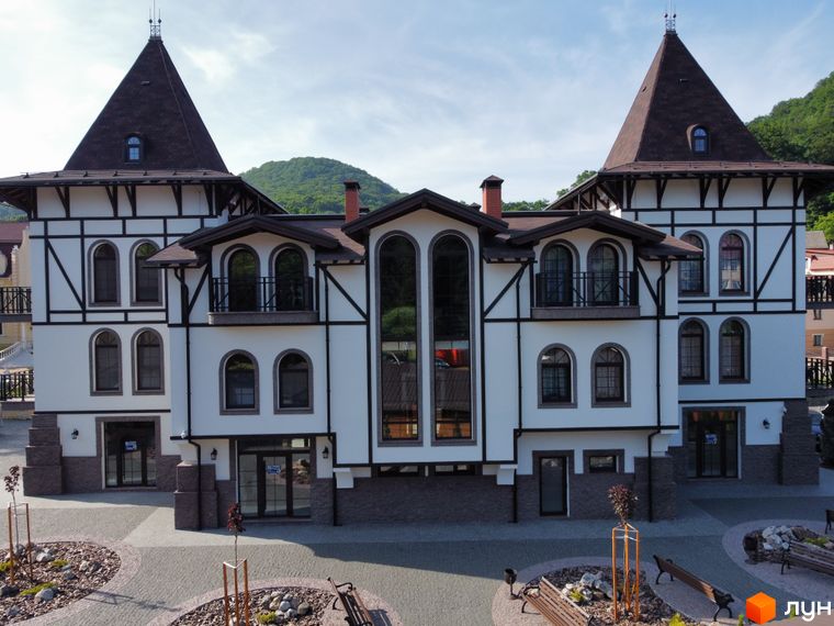 Житловий комплекс Shayan lux house з фасадом у стилі шале та прибудинковою територією з ландшафтним дизайном. Зовнішній вигляд будівлі з вежами та арочними вікнами.