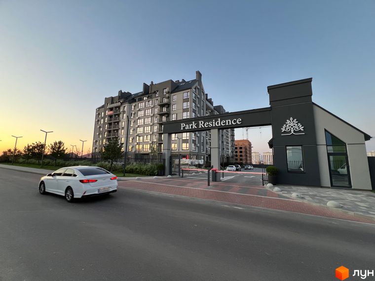 Житловий комплекс Park Residence з фасадом сірого кольору та скляними балконами. Прибудинкова територія з дорогою та в'їзною аркою.