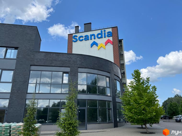 Будівельний проєкт Scandia з фасадом з темної цегли та великими вікнами. Поруч зелені дерева та парковка.