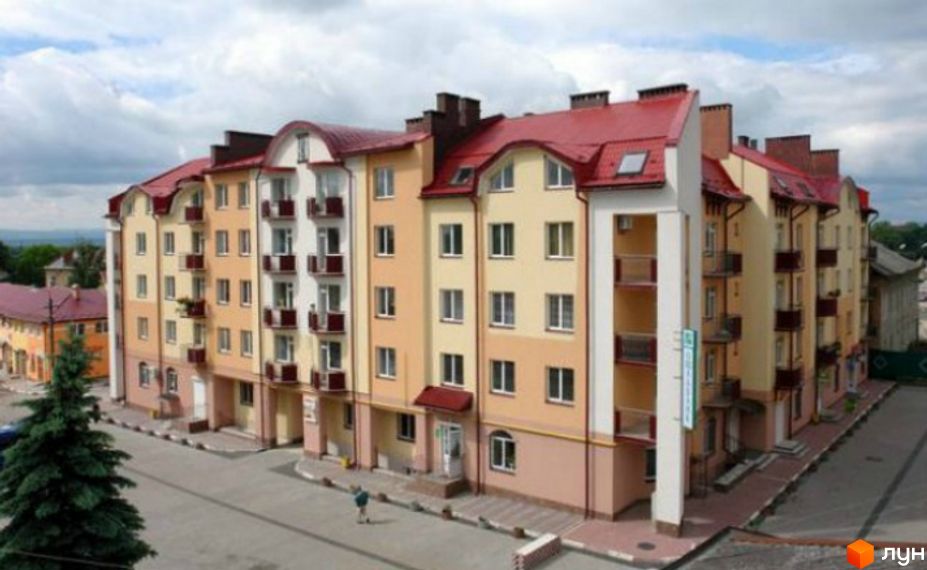Фасад новобудови на вул. Шевченка, 5, з балконами та червоним дахом. Прибудинкова територія з деревами та дорогою.