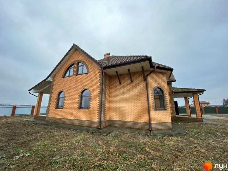 Котеджне містечко Колонщина: цегляний будинок з арочними вікнами та прибудинковою територією під сірим небом.