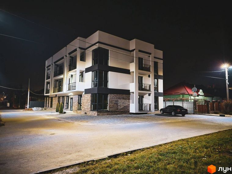 Зображення фасаду Житлового комплексу Premium House вночі. На передньому плані асфальтована дорога та припаркований автомобіль.
