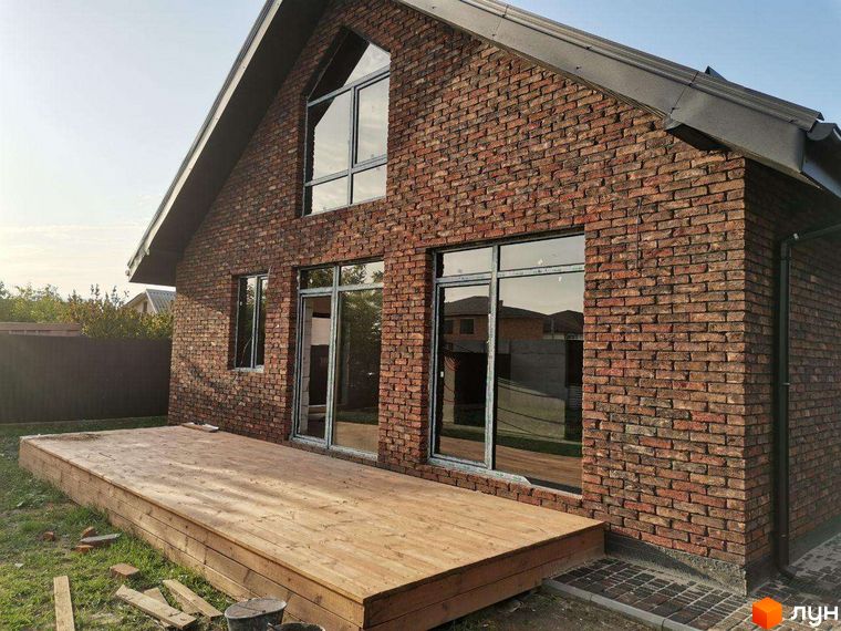 Котеджне містечко КМ Одноповерховий Київ - Дніпро. Фасад будинку з червоної цегли, великі вікна та дерев'яна тераса.