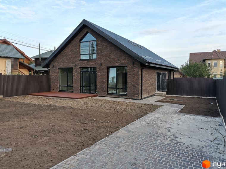 Котеджне містечко КМ Одноповерховий Київ - Дніпро: цегляний будинок з великими вікнами та терасою на тлі зеленого двору та паркану.