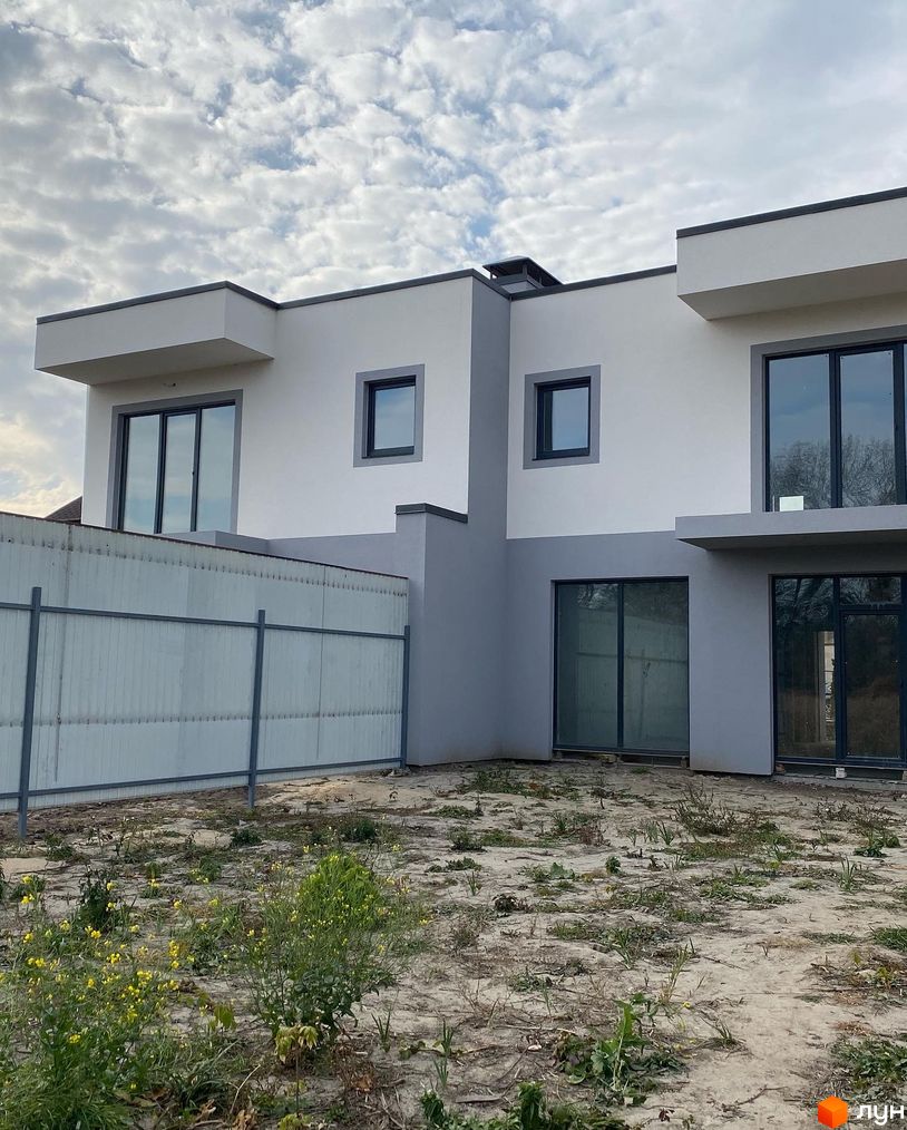 Зовнішній вигляд котеджного містечка Чапаєвка з сірими та білими фасадами, великими вікнами та прибудинковою територією з невисокою рослинністю.