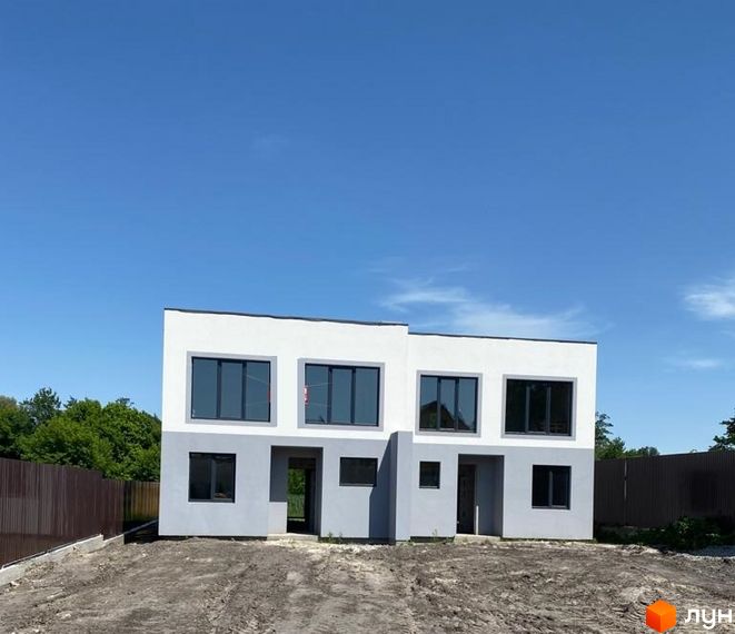 Котеджне містечко Чапаєвка: двоповерхові будинки з великими вікнами та сірим оздобленням фасаду на тлі блакитного неба. Територія навколо будинку вкрита ґрунтом.