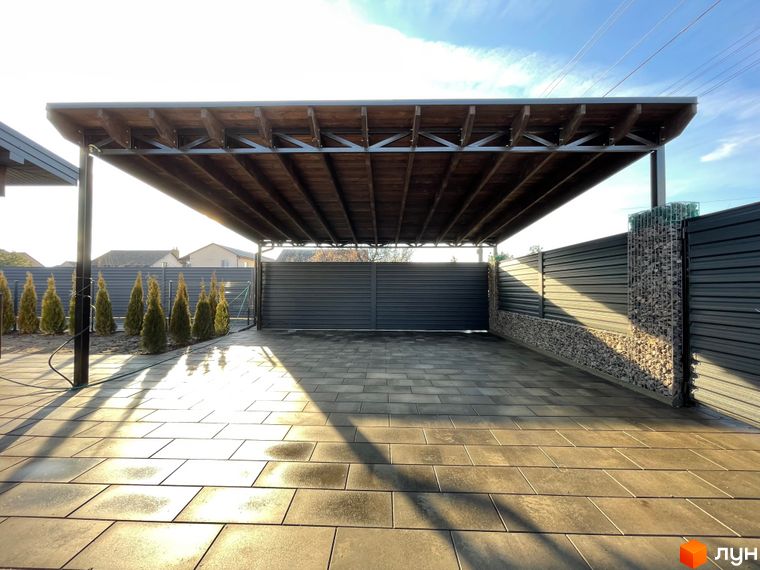 Навіс для авто з дерев'яною обробкою та бруківка на подвір'ї житлового комплексу по вул. Мазепи. Прибудинкова територія має огорожу з габіонами.
