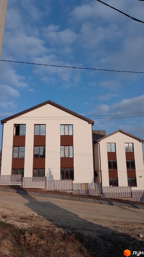 Зовнішній вигляд новобудови на вул. Лісова з білими стінами та коричневими вікнами. Перед будинком розташований паркан та дорога.