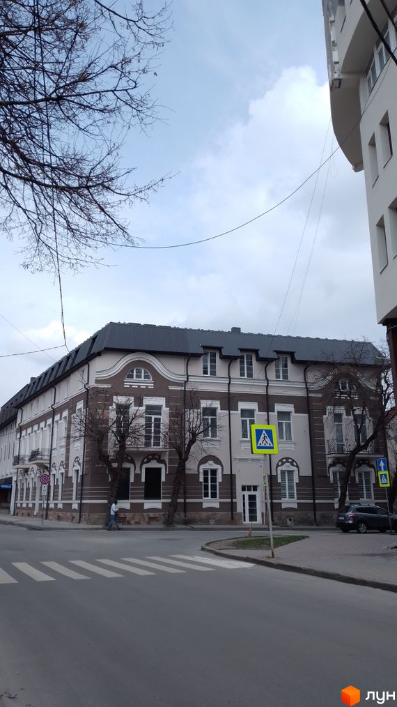 Будинок на вулиці Івана Франка, 20, з коричнево-білим фасадом та темним дахом. Поруч розташована прибудинкова територія з пішохідним переходом.