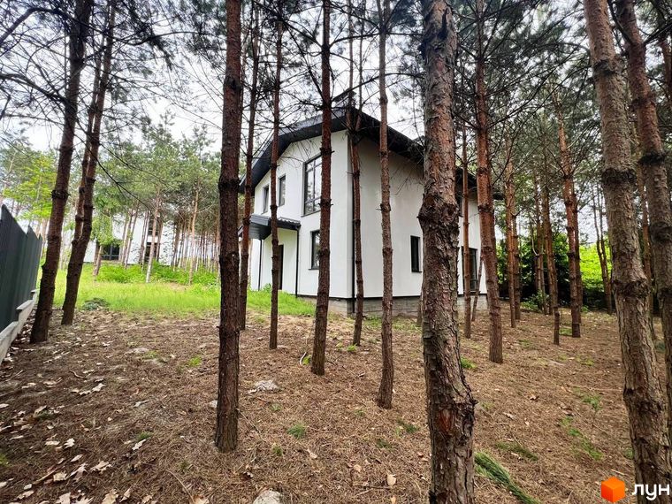 Зображення будинку в Котеджному містечку GREEN CLUB, оточеного сосновим лісом. Навколо будинку видно опале листя та хвою.