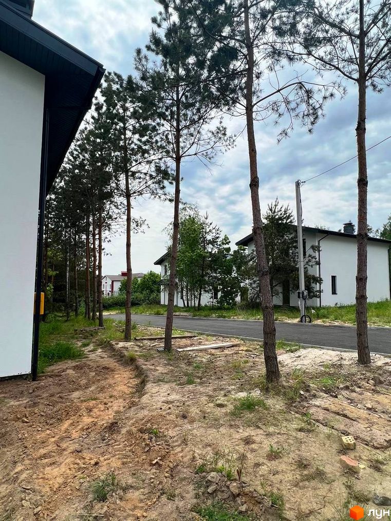 Зовнішній вигляд будинку в Котеджному містечку GREEN CLUB. Навколо будинку дерева та піщаний ґрунт.