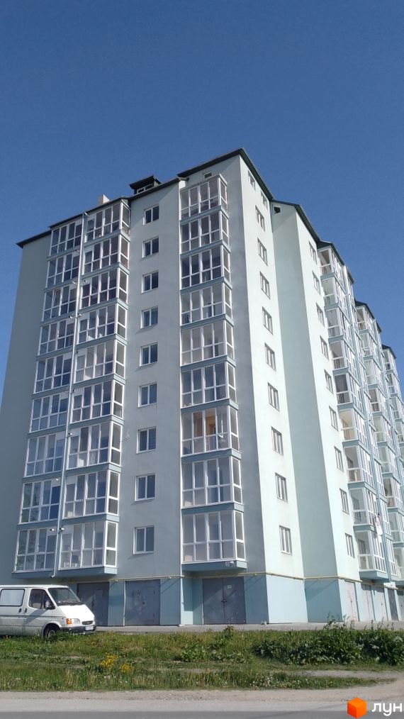 Багатоповерховий житловий будинок світло-сірого кольору з численними заскленими балконами, розташований на вул. Зелена, 48. Перед ним зелена трава та фургон.