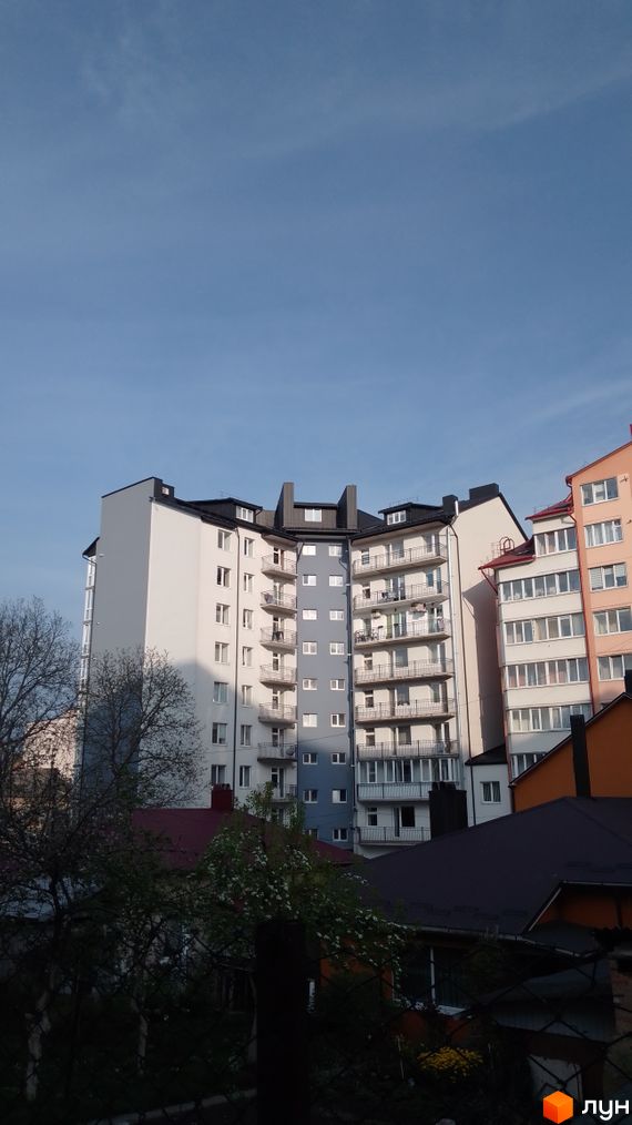 Багатоповерховий житловий будинок з біло-сірим фасадом та балконами на вул. Крушельницької, 55. На передньому плані видно дерева та дахи.