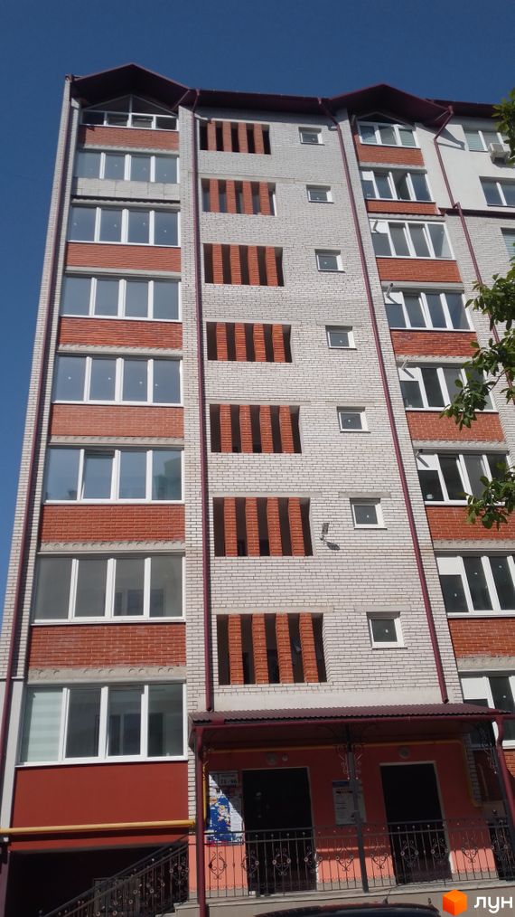 Багатоповерхова новобудова на вул. Рєпіна, 34, з фасадом з світлої цегли, червоними вставками та білими вікнами. Вхідна група має козирок.