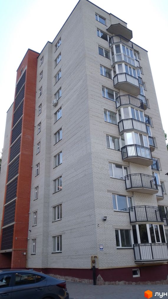 Будинок на вулиці Патріарха Любомира Гузара (Чалдаєва), 8а, з білої цегли та червоною вставкою з вікнами. Навколо будинку бруківка та зелені насадження.
