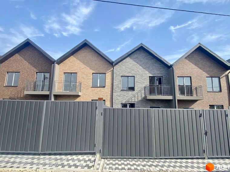 Фасад Таунхаусів „Чемпіон“ з цегляною кладкою різних відтінків, балконами та металевим парканом, що огороджує територію з бруківкою.