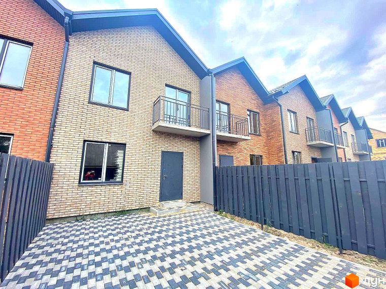 Ряд двоповерхових таунхаусів „Чемпіон“ з цегляними фасадами та балконами. Перед будинками викладена бруківка та встановлений темний паркан.