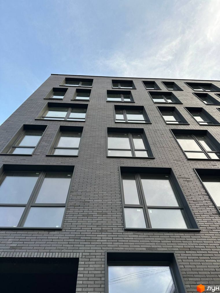 Фасад Житлового комплексу ArtHof виконаний з темно-сірої цегли з великими вікнами. Зображено частину будинку під блакитним небом.