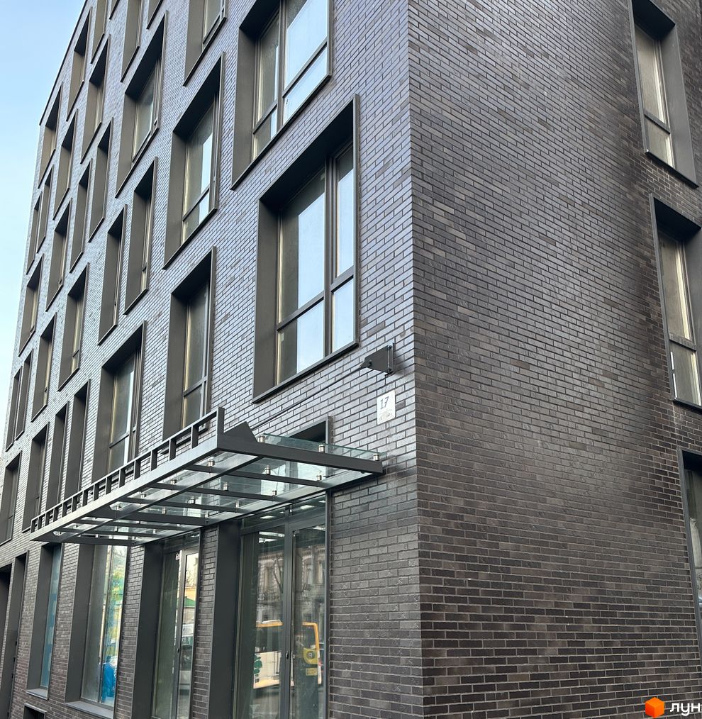 Фасад новобудови ArtHof з темної цегли та великими вікнами. Зовнішній вигляд будинку з скляним навісом над входом.