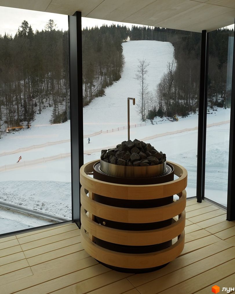 Апарт-комплекс Mountain Residence з панорамними вікнами, що виходять на засніжений гірськолижний схил з лісом. На передньому плані видно елементи інтер'єру.