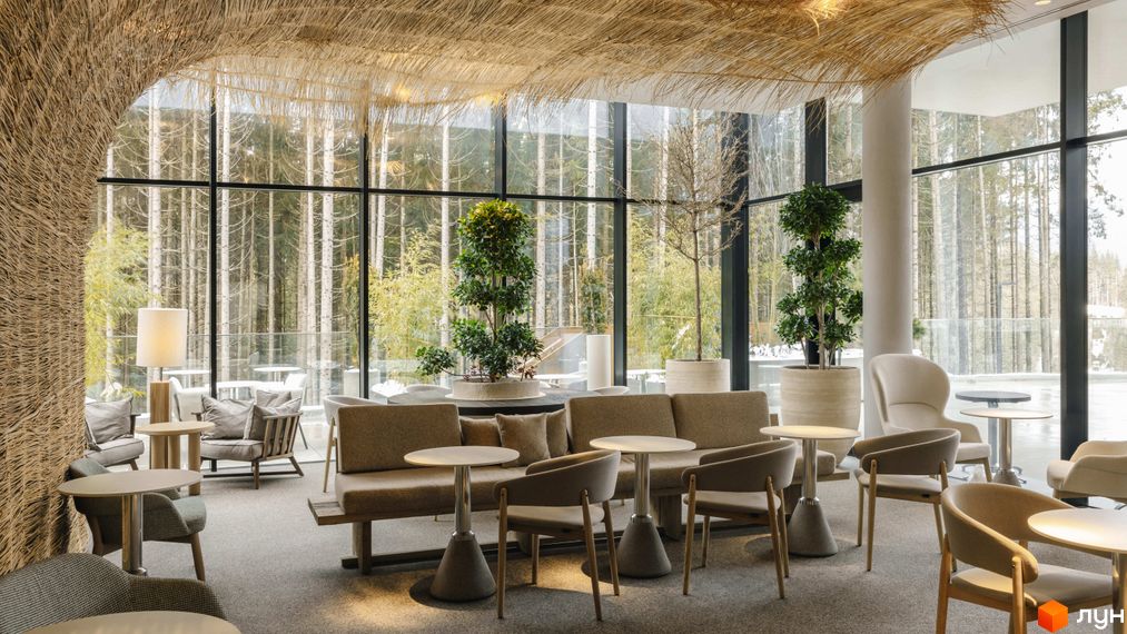 Інтер'єр апарт-комплексу Mountain Residence з панорамними вікнами та видом на ліс. Затишна зона відпочинку з диванами та кріслами біля каміна.