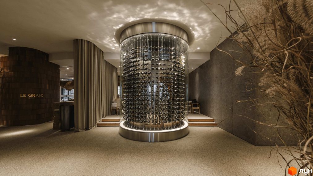 Апарт-комплекс Mountain Residence з вражаючою циліндричною винною шафою в центрі просторого залу. Інтер'єр оформлений у природних тонах з акцентом на дерево та текстиль.