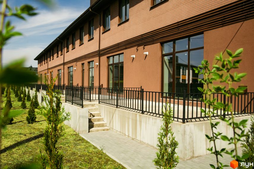 Будівля Житлового комплексу клубного типу Обрій з цегляним верхом та пофарбованим низом, великими вікнами. Прибудинкова територія має зелений газон з рядами молодих дерев.