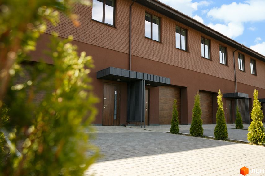 Житловий комплекс клубного типу Обрій: двоповерхові таунхауси з коричневою цегляною та штукатурною обробкою, дерев'яними воротами. Прибудинкова територія з бруківкою та хвойними деревами.