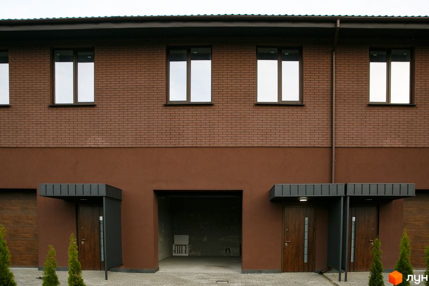 Фасад житлового комплексу клубного типу Обрій з коричневої цегли та штукатурки. Вхідні двері, гаражі, бруківка та зелені насадження біля будинку.