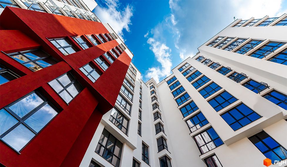 Житловий комплекс Comfort House - фасади будівель з червоними та білими елементами, великі вікна з синіми склопакетами, вид знизу на тлі блакитного неба з хмарами.