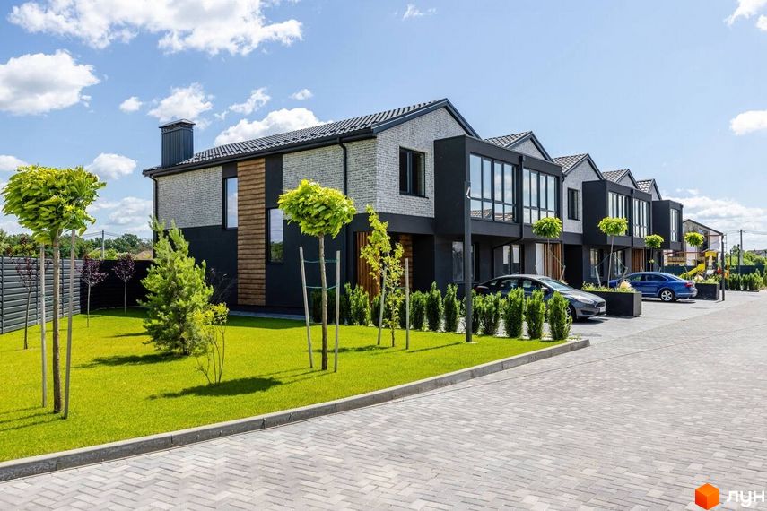 Котеджне містечко Romankiv Village: фасади будинків з сірої цегли та чорних панелей, великі вікна, доглянутий газон та дерева.