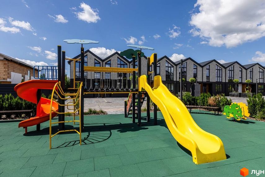 Дитячий майданчик з гірками та гойдалками на фоні котеджного містечка КМ Romankiv Village. Сучасні будинки з панорамними вікнами.