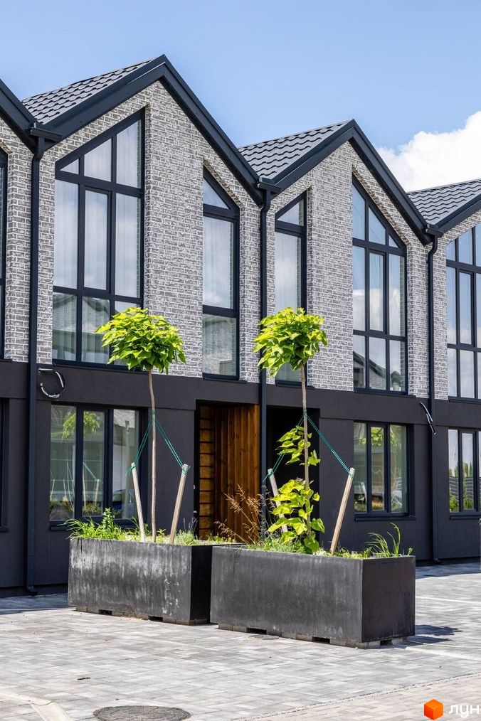 Котеджне містечко Romankiv Village: фасади будинків з сірої цегли та великими вікнами, прибудинкова територія з рослинами у великих бетонних клумбах.