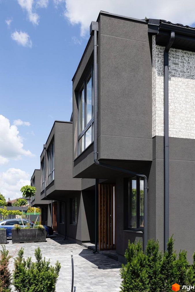 Котеджне містечко Romankiv Village. Зовнішній вигляд будинків з сірим фасадом та білою цегляною кладкою, прибудинкова територія з бруківкою та зеленими насадженнями.