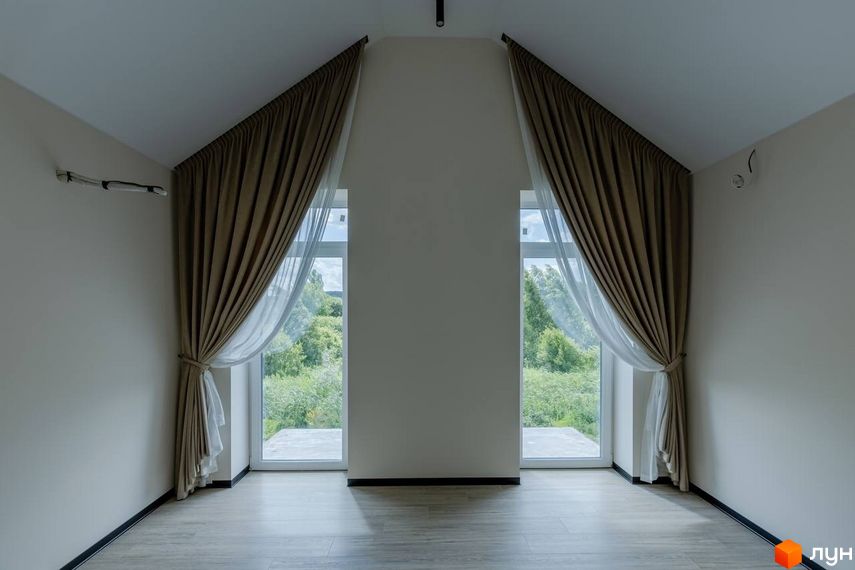 Інтер'єр кімнати з двома великими вікнами, що виходять на зелену територію, в котеджному містечку КМ Romankiv Village. Завіси з тюлем створюють затишок.