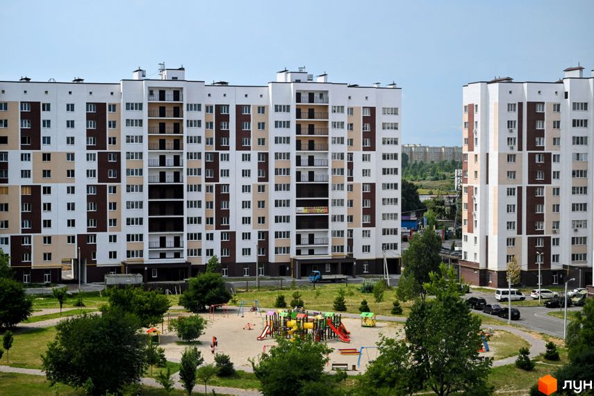 Житловий комплекс Сади Вишневі: багатоповерхові будинки з біло-коричневим фасадом та дитячим майданчиком на прибудинковій території.