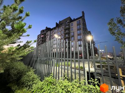 Житловий комплекс Park Residence з фасадом з сірих та бежевих панелей, вікнами та балконами, на фоні вечірнього неба. На прибудинковій території встановлено паркан та зелені насадження.