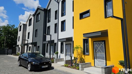 Таунхауси New Smart 9: фасади будинків у сірих та жовтих кольорах, з чорними вікнами, перед будинками розташована бруківка та зелені насадження.