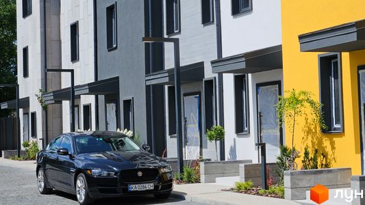 Таунхауси New Smart 9 з чорним авто на тлі біло-жовтих будинків. Зовнішній вигляд таунхаусів та прибудинкова територія.