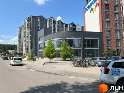 Зовнішній вигляд житлового комплексу Scandia з багаторівневими фасадами та панорамними вікнами. На прибудинковій території розташовані дерева та парковка з велосипедами.