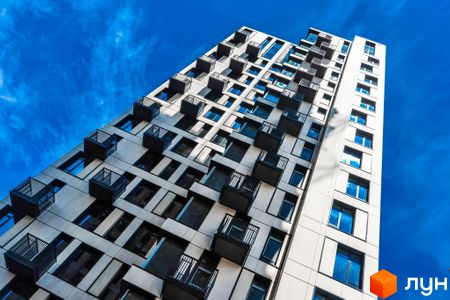 Зовнішній вигляд новобудови ЖК TRIIINITY з численними балконами та вікнами на тлі блакитного неба. Фасад будівлі має геометричний дизайн.